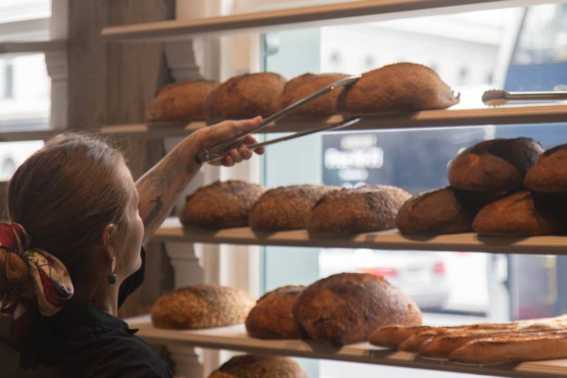 A worker selecting a loaf from shelves of bread at Daily Bread, Britomart.